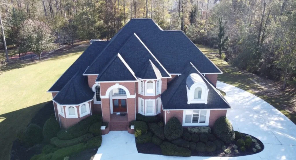 brick home in Alpharetta with black roof and roundabout driveway in front of wooded area